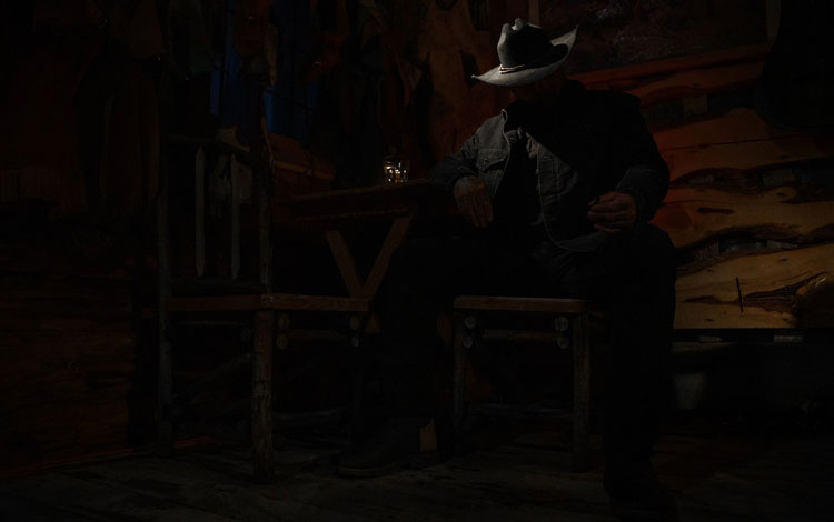 Cowboy sitting in a chair in the dark.